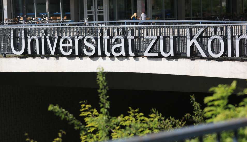 Das Foto zeigt den Schriftzug "Universität zu Köln" an einer Fußgängerbrücke in Köln.