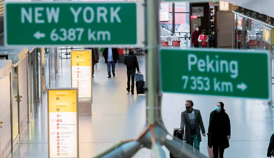 Zwei Personen am Flughafen vor Schildern mit der Distanz zu New York und Peking