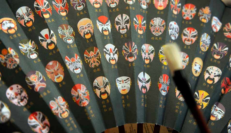 Chinesischer Fächer mit aufgedruckten bunten Gesichtern und Schriftzeichen