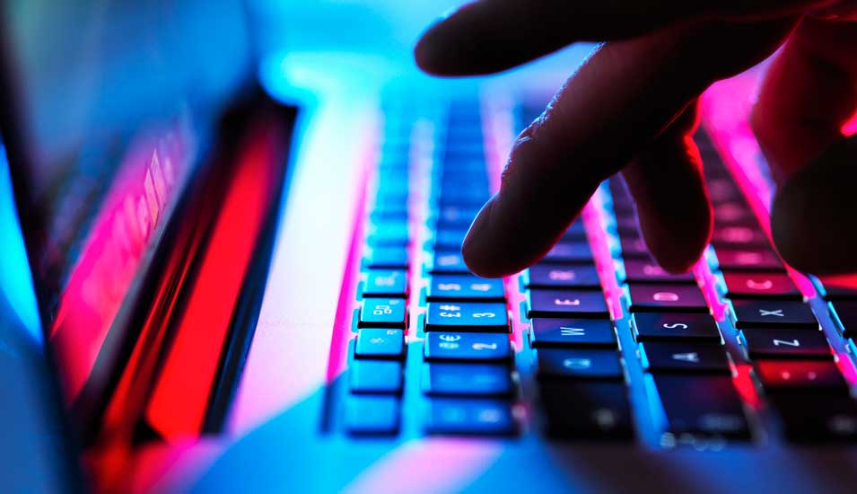 Symbolbild "Cyberkriminalität": Dunkle Hand lippt auf Laptoptastatur.