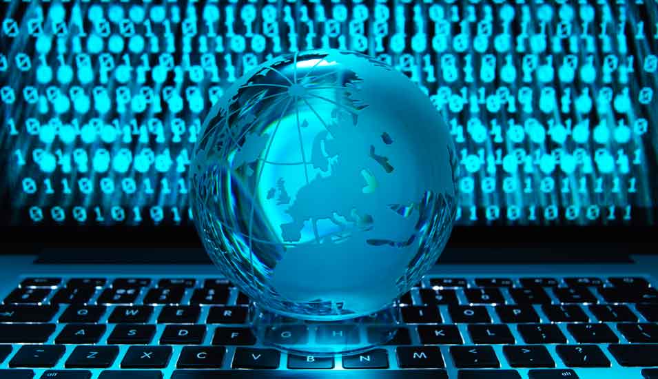 Gläserne Weltkugel vor einem Laptop auf dem Binärcode abgebildet ist (Symbolbild "Cyberkriminalität"). 