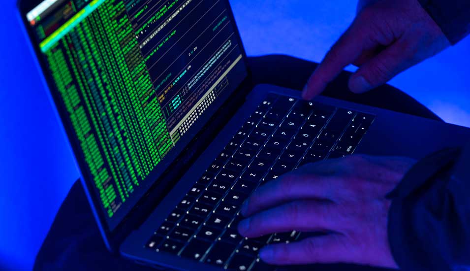 Symbolbild Cyberkriminalität mit einem Laptop und Händen vor dunklem Hintergrund.