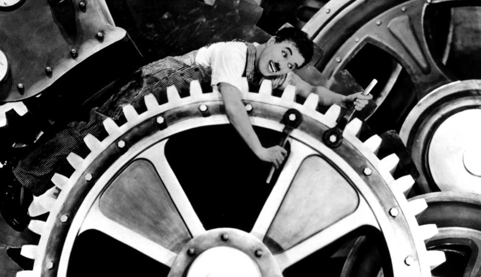Das Foto zeigt Charlie Chaplin auf ein Zahnrad gespannt aus dem Film "Moderne Zeiten"