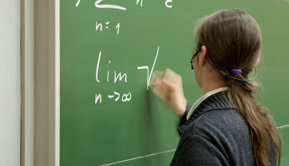 Das Foto zeigt eine Professorin, die mathematische Formeln auf eine Tafel schreibt