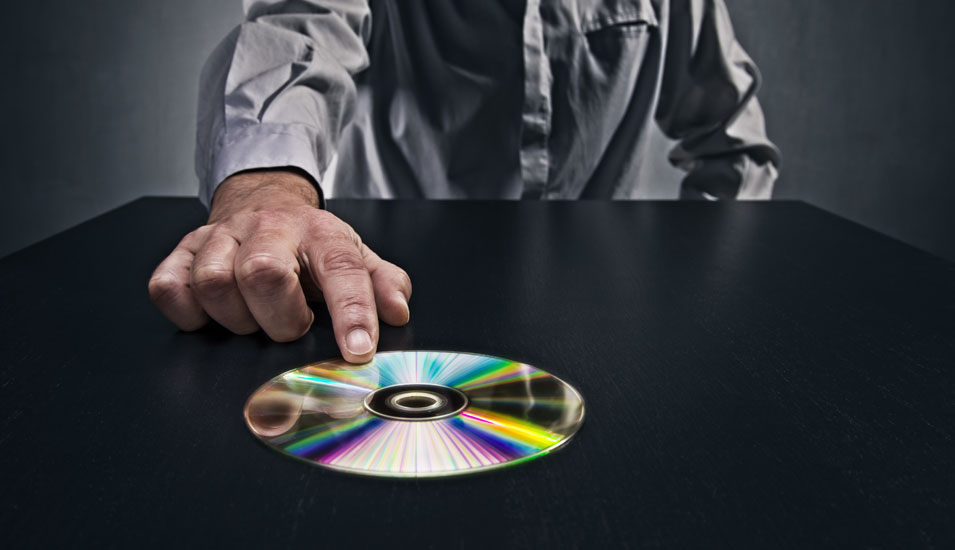 Das Foto zeigt einen Mann, der eine CD-ROM über einen Tisch schiebt.