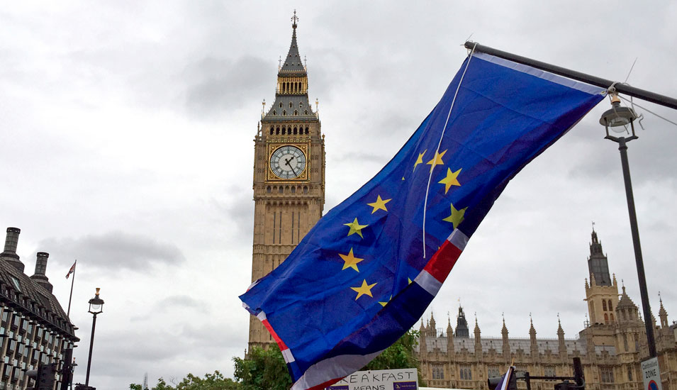 Big Ben in Großbritannien, im Vordergrund eine beidseitig bedruckte Flagge von EU und Großbritannien