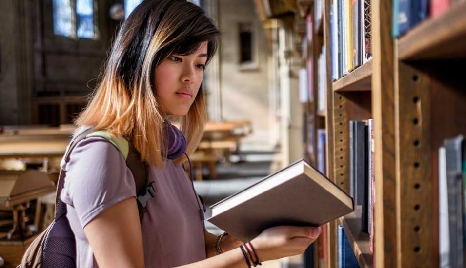 Chinesische Studentin schaut in Bibliothek in ein Buch