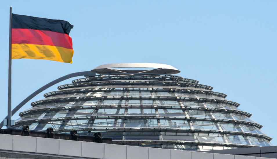 Das Foto zeigt die Kuppel des Reichstages in Berlin mit wehender Deutschlandfahne