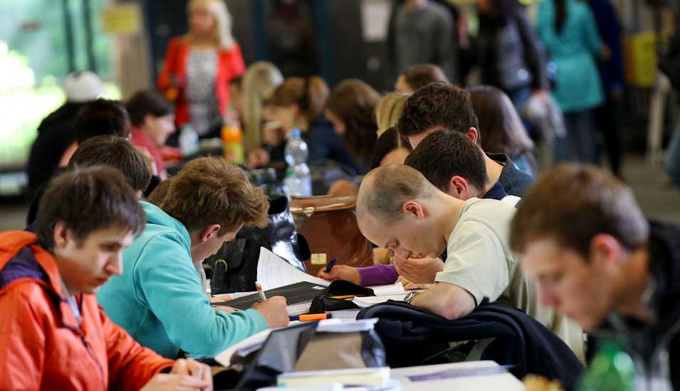 Das Foto zeigt Studenten der Universität Köln an einem langen Tisch mit Büchern.