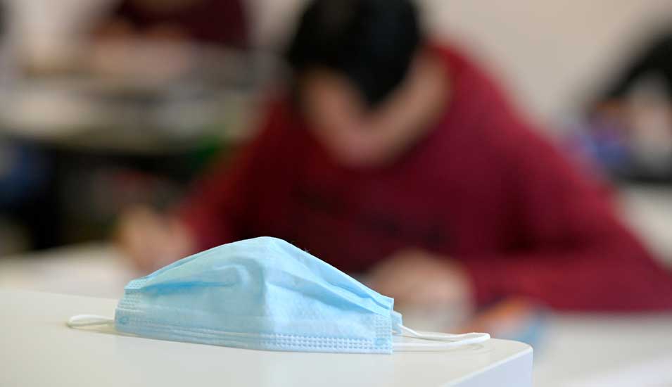 Mundschutzmaske auf einem Tisch in einem Klassenraum mit Schülern