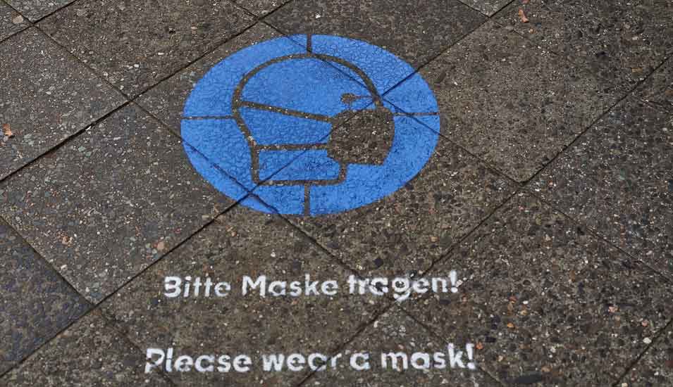 Hinweisschild zur Maskenpflicht auf einem Bürgersteig auf deutsch und englisch