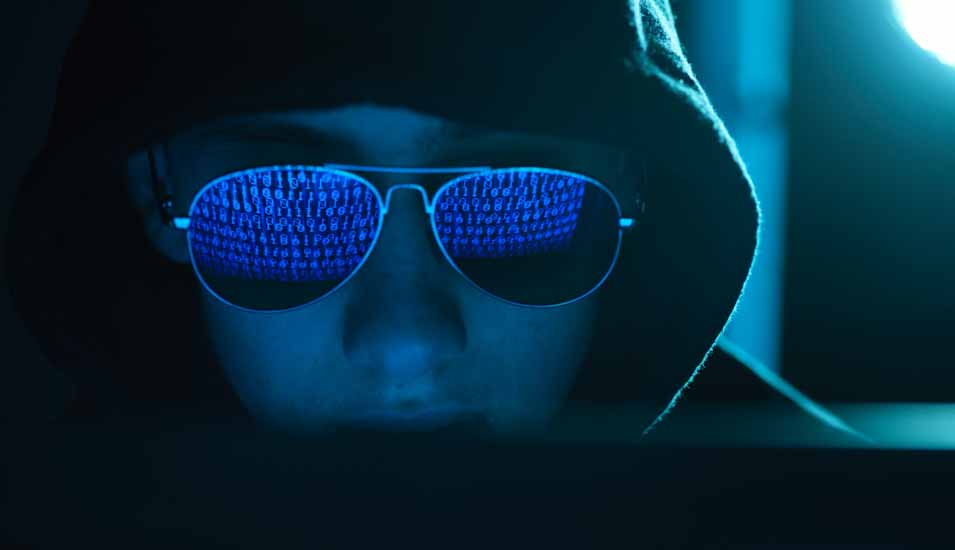 Computercode spiegelt sich in der Sonnenbrille eines Hackers mit schwarzem Kapuzenpullover