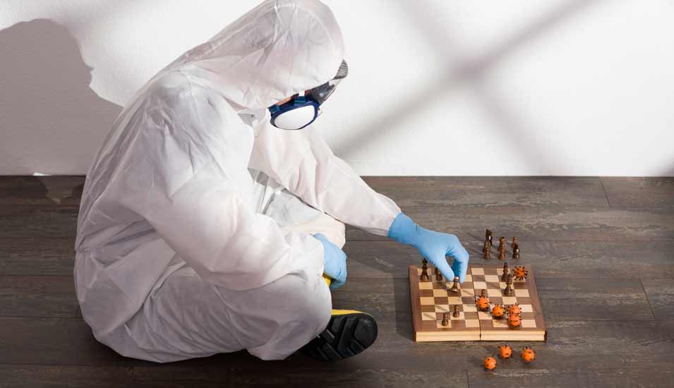 Person in einem Schutzanzug spielt Schach mit Viren