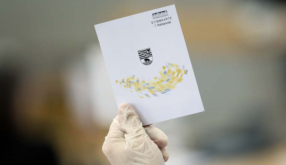 Landtagsabgeordneter mit Gummihandschuhen hält während der Landtagssitzung eine Stimmkarte in die Höhe