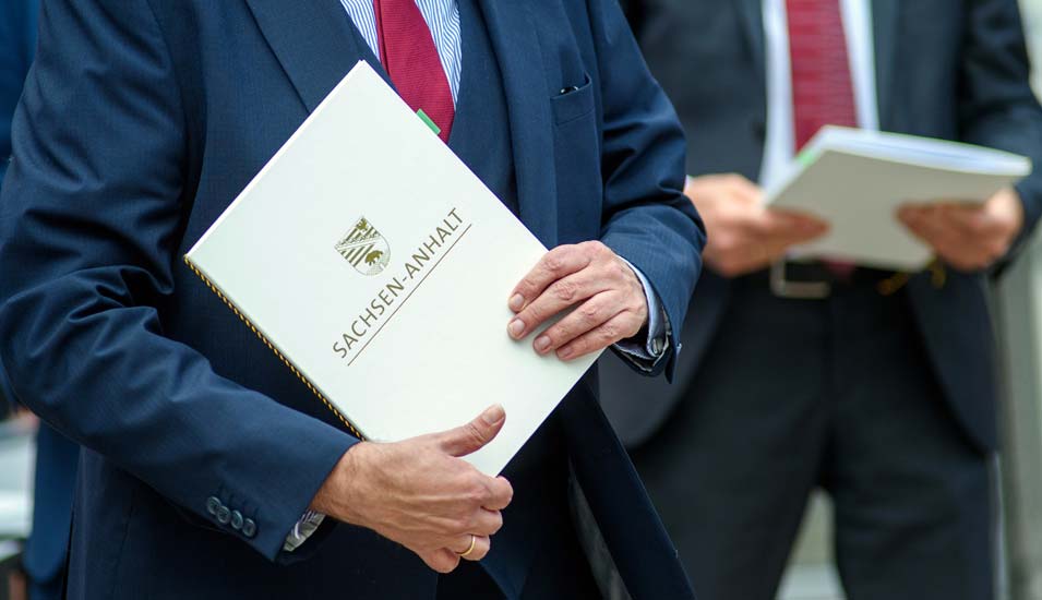 "Sachsen-Anhalt" steht in goldener Schrift auf einer weißen Mappe in den Händen von Sachsen-Anhalts Wissenschaftsminister Willingmann