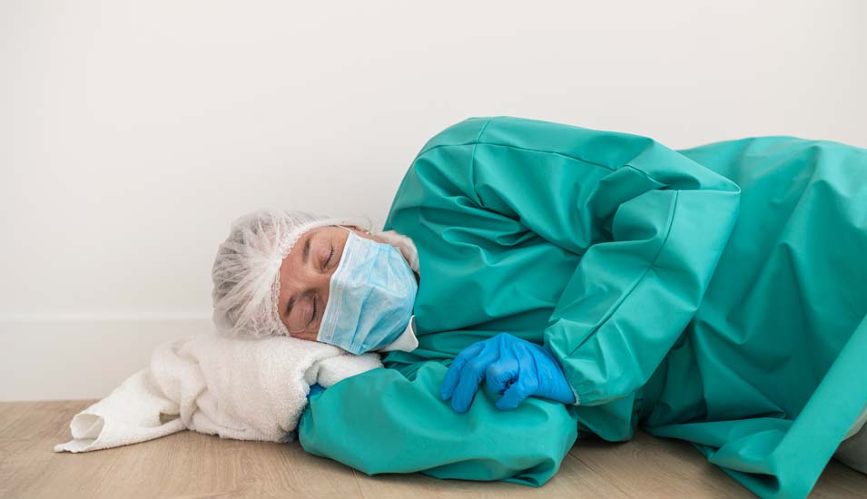 erschöpfte Ärztin in Schutzkleidung liegt auf dem Boden und schläft