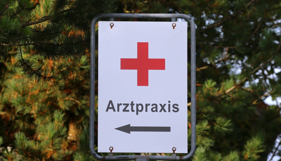 Das Foto zeigt ein Schild mit rotem Kreuz zu einer Arztpraxis.