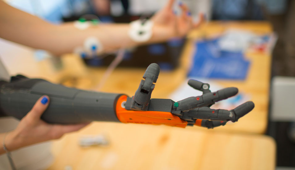 Forscherin hält eine Roboterhandprothese und bewegt diese mit ihrer anderen Hand.