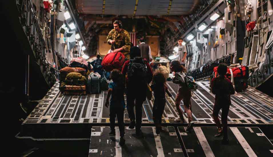 Das Bild blickt ins innere eines Militärflugzeugs, Evakuierte betreten es durch die Laderampe.