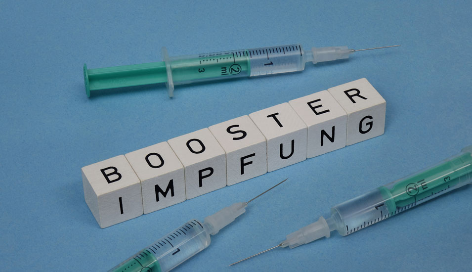 Spritzen und der Schriftzug "Boosterimpfung" auf Buchstabenwürfeln.