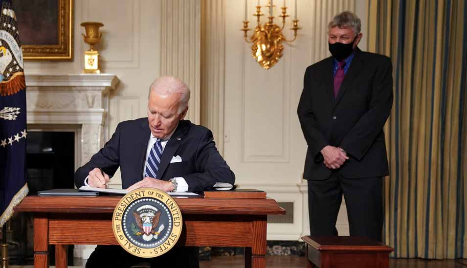 US-Päsident Joe Biden unterzeichnet ein Dokument, während sein wissenschaftlicher Berater Eric Lander hinter ihm steht