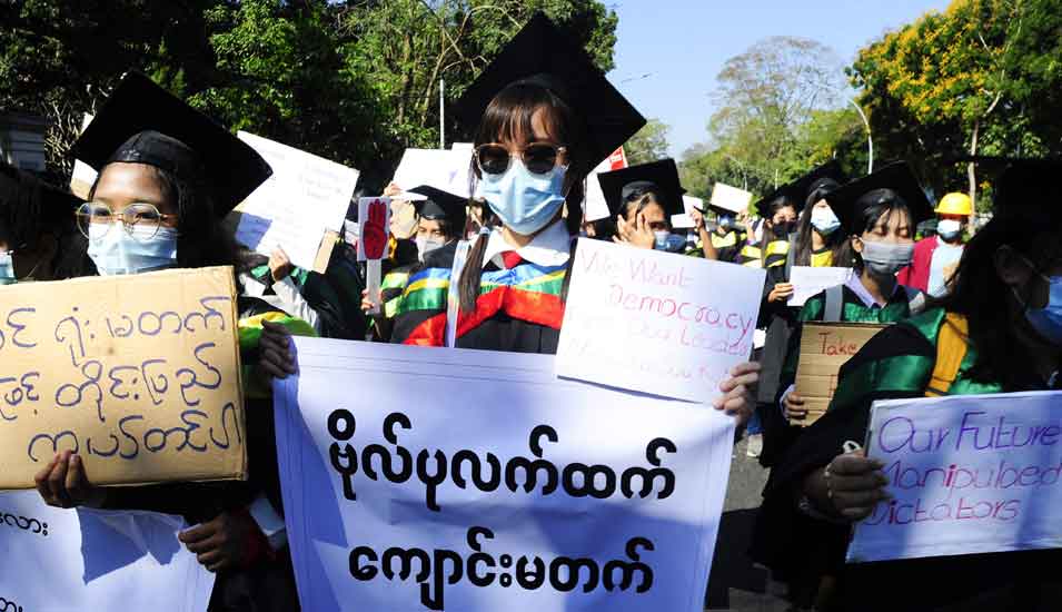Studierende in Abschlussroben mit Plakaten bei einem Protestmarsch gegen die Militärregierung in Myanmar im Februar 2021