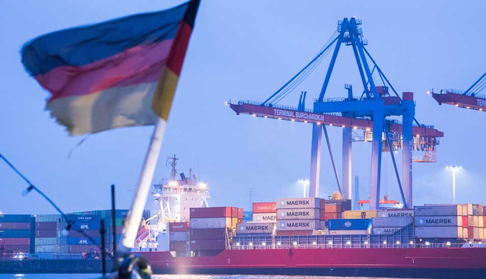 Containerschiff im Hafen, im Vordergrund eine deutsche Flagge