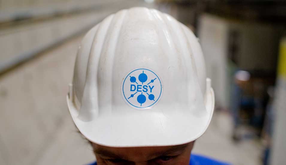 ein Mitarbeiter trägt das Logo des Desy auf seinem weißen Helm, während er im Teilchenbeschleuniger-Tunnel des Röntgenlaser-Projekts European XFEL steht