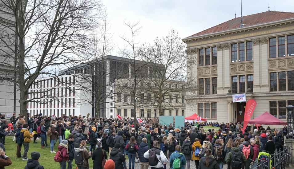 Eine Ansammlung Demonstranten vor der Universität Halle. Man sieht sie nur vor hinten.