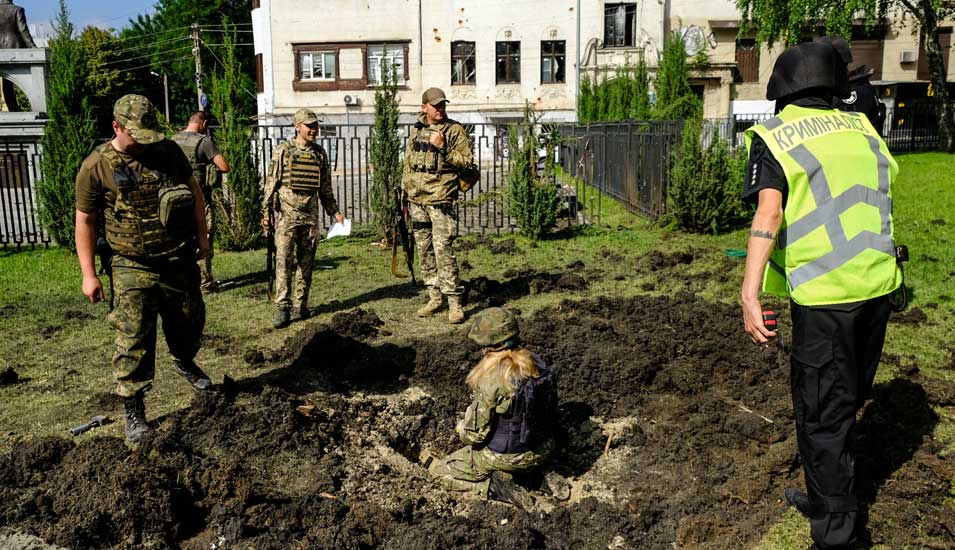 Ukrainische Offizielle im Garten einer Universität in Charkiw. Sie inspizieren ein Einschlagsloch.