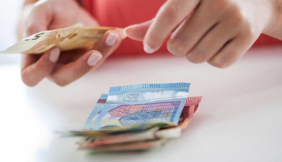 Frau legt einen 50-Euro-Schein auf eine Stapel Geldscheine