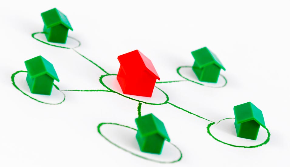 Smybolbild für vernetzte Organisationen: Grüne Spielhäuser stehen um ein rotes Haus herum auf einem aufgemalten Netzwerk.