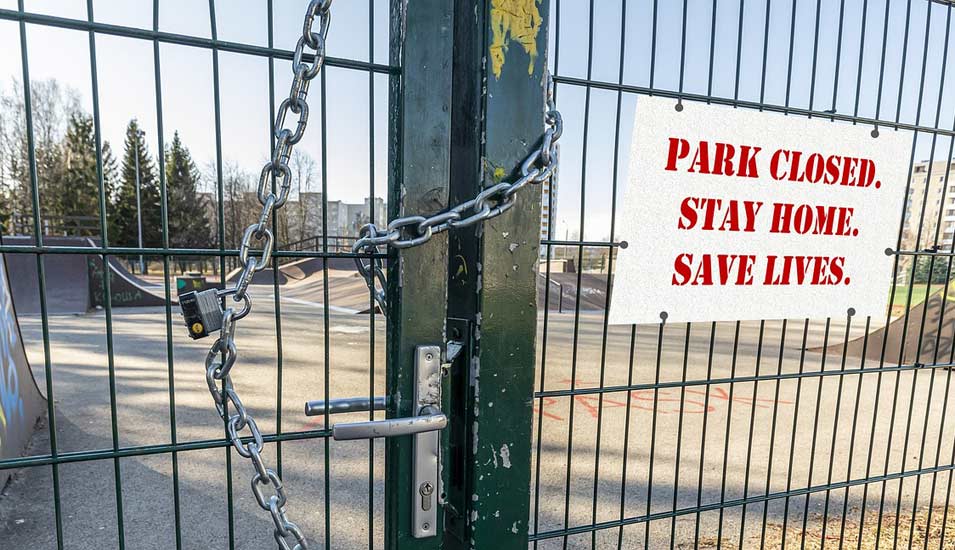 Das grüne Metalltor eines Parks ist mit einer Eisenkette verschlossen und ein Schild weist auf Corona-Lockdown hin. 