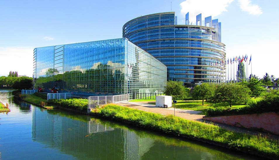 Ein rundes, großes Bürogebäude an einem Fluss im Sonnenschein: Es ist das europäische Parlament in Straßburg