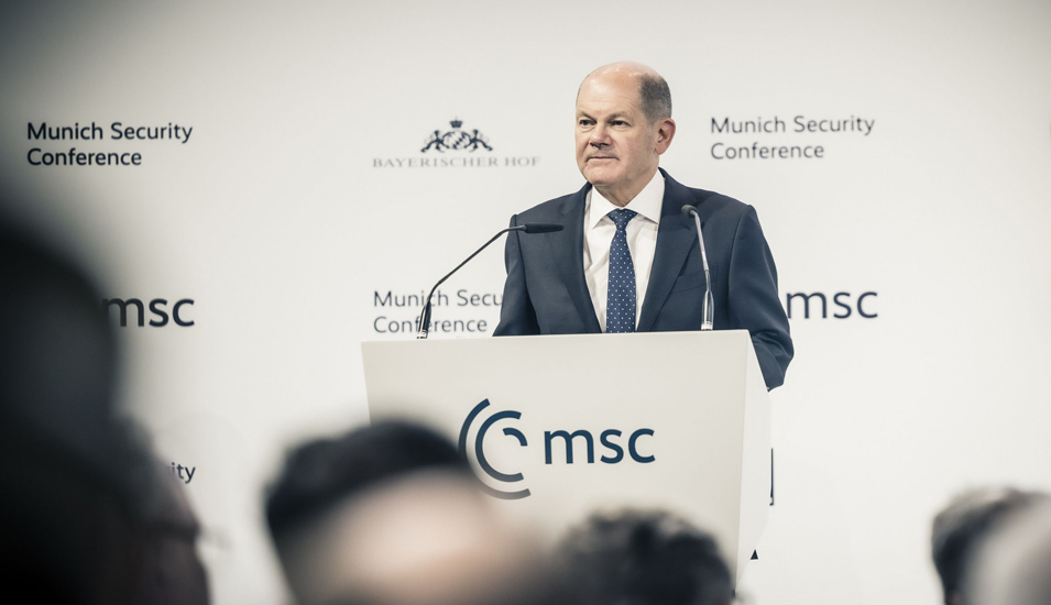Vor einer weißen Wand mit der Aufschrift "Münchner Sicherheitskonferenz" ist Bundeskanzler Olaf Scholz in ein Mikrofon sprechend zu sehen.