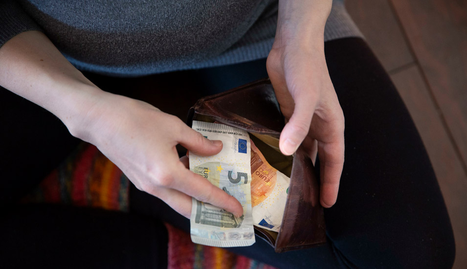 Ein Portemonnaie ist zu sehen aus dem eine Hand einen Fünf- und einen Zehn-Euro-Schein rausholt. 
