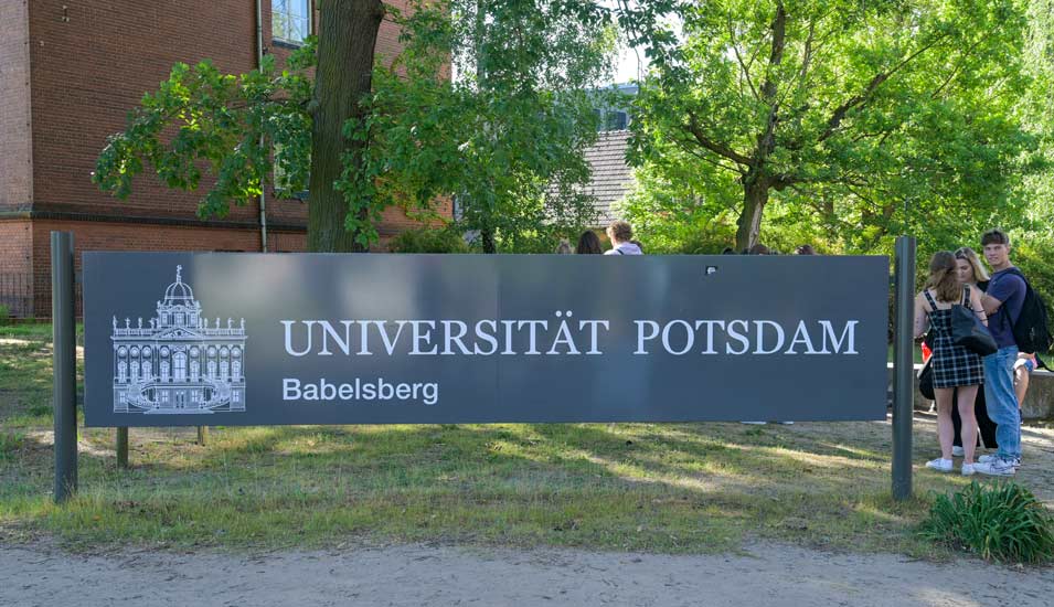 Namensschild der Universität Potsdam vor einem sandsteinfarbenen Gebäude