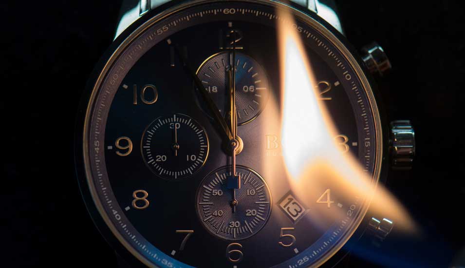 Das Foto zeigt eine Uhr, kurz vor zwölf, mit einer Flamme.