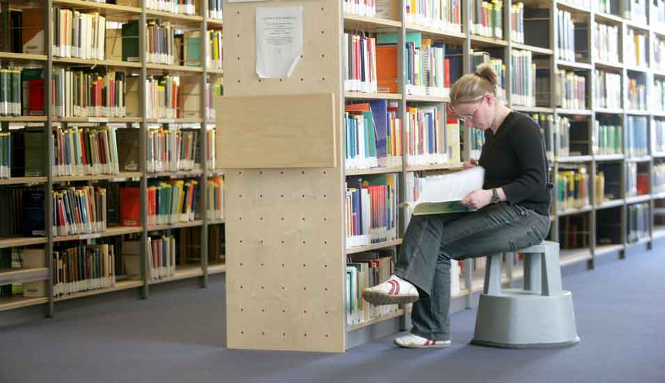 Das Foto zeigt eine Studentin vor einem Bücherregal in der Universitätsbibliothek Jena.