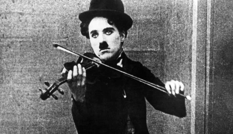 Das Foto zeigt Charlie Chaplin als Tramp mit einer Geige