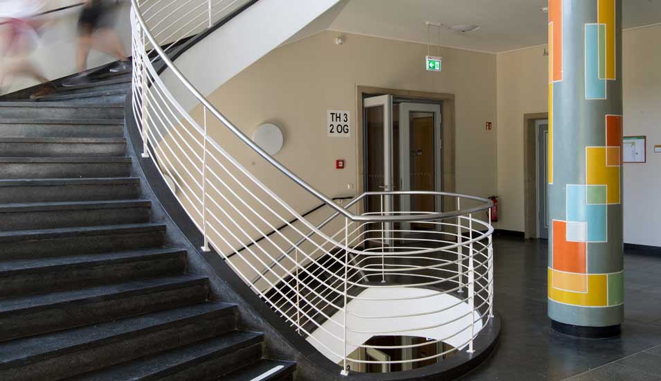 Das Foto zeigt einen Treppenaufgang der TU Dresden mit einer bunten Säule.