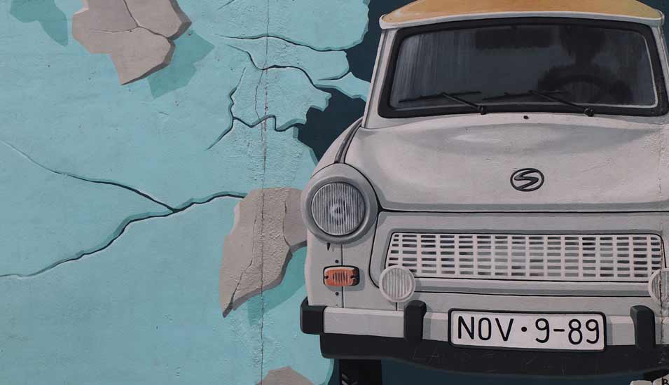 Graffiti eines Trabis, der durch die Berliner Mauer bricht