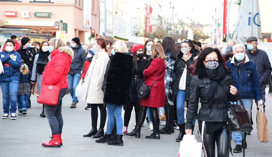 Menschen mit Masken stehen Schlange in einer Einkaufsstraße