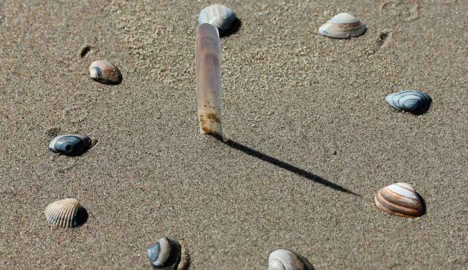 Ziffernblatt einer Uhr aus Muscheln gelegt an einem Sandstrand