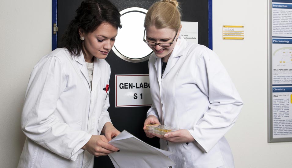 zwei Wissenschaftlerinnen unterhalten sich im Labor über eine Publikation gebeugt