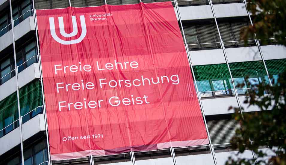 Ein rotes Plakat mit der Aufschrift "Freie Lehre, Freie Forschung, Freier Geist" hängt an einem Gebäude der Universität Bremen. 