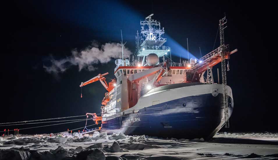 Aufnahme des Forschungsschiffes "Polarstern" vor dunklem Hintergrund. Es wird durch seine Scheinwerfer beleuchtet.