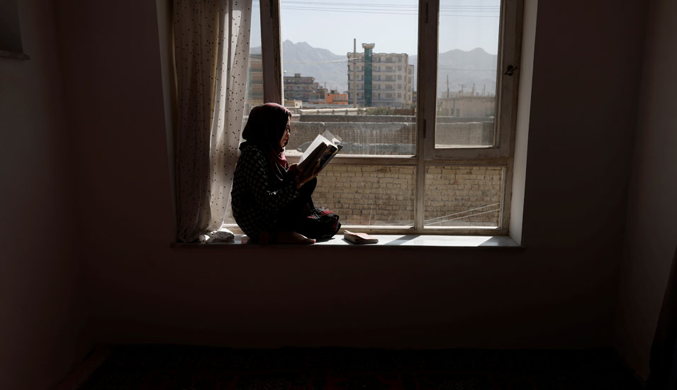 Eine afghanische Studentin sitzt zu Hause am Fenster und liest, in ihre Universität darf sie wegen der Taliban nicht zurückkehren.
