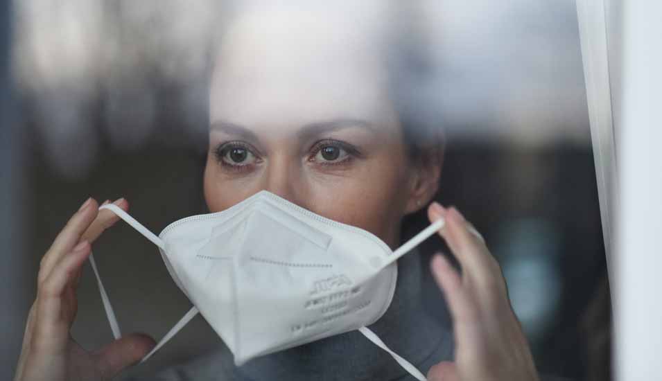 Eine Frau setzt eine Mund Nasenschutz Maske vom Typ FFP2 auf