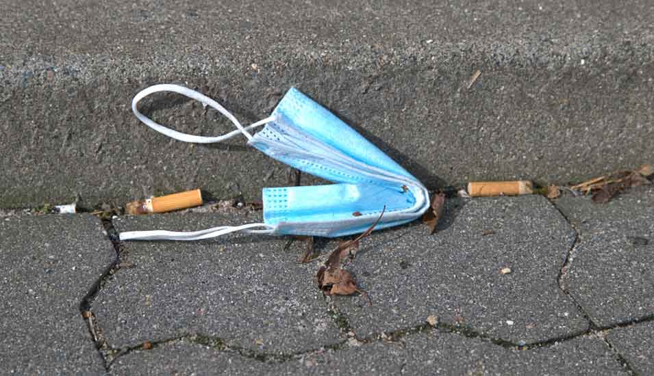 Eine Maske liegt weggeworfen zwischen Zigarettenstummeln auf einer Straße.